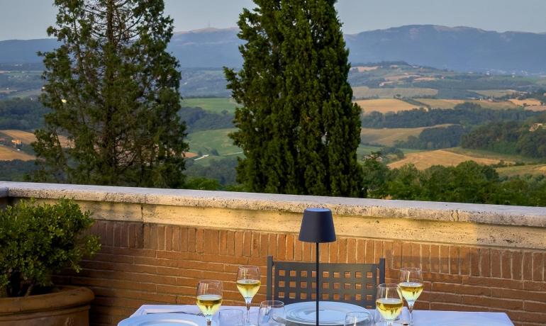 Cena romantica all'aperto con vista su colline e cipressi al tramonto.