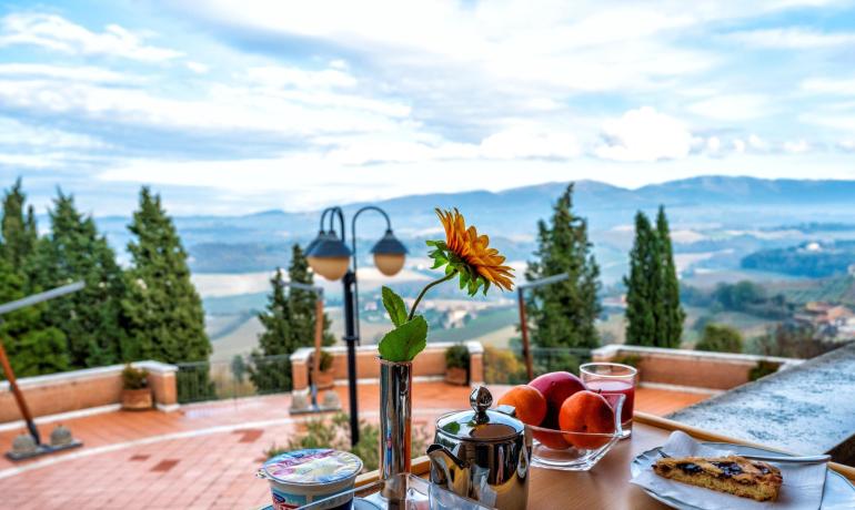 Colazione panoramica con dolci, frutta e vista mozzafiato su colline e cipressi.