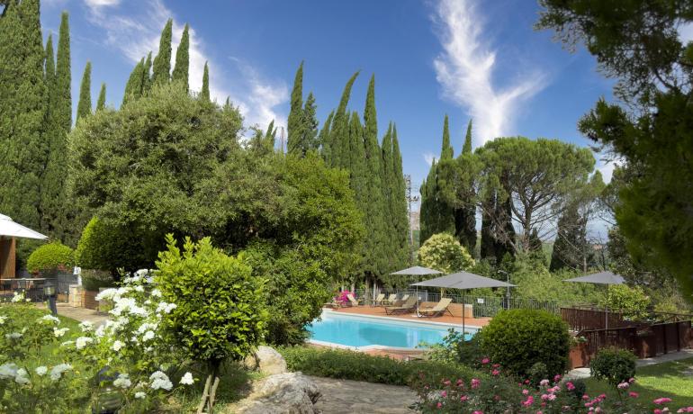 Giardino lussureggiante con piscina, fiori colorati e alberi imponenti sotto un cielo sereno.
